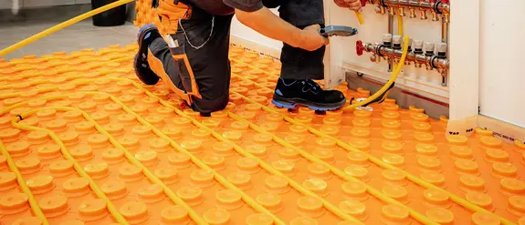 Um profissional corta um tubo de aquecimento com o comprimento necessário para o circuito de climatização e coloca-o numa placa com nódulos BEKOTEC de cor laranja da Schlüter-Systems.