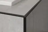 Canto de uma borda de banheira revestida com azulejos, com perfil de remate preto e cer&acirc;mica cinzento claro