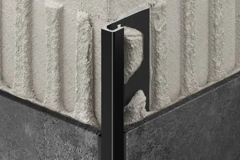 Vista detalhada do perfil de proteção de aresta Schlüter-QUADEC-AC com acabamento TRENDLINE na cor MGS preto grafite mate ante um canto exterior de parede revestido com cerâmica em cor antracite