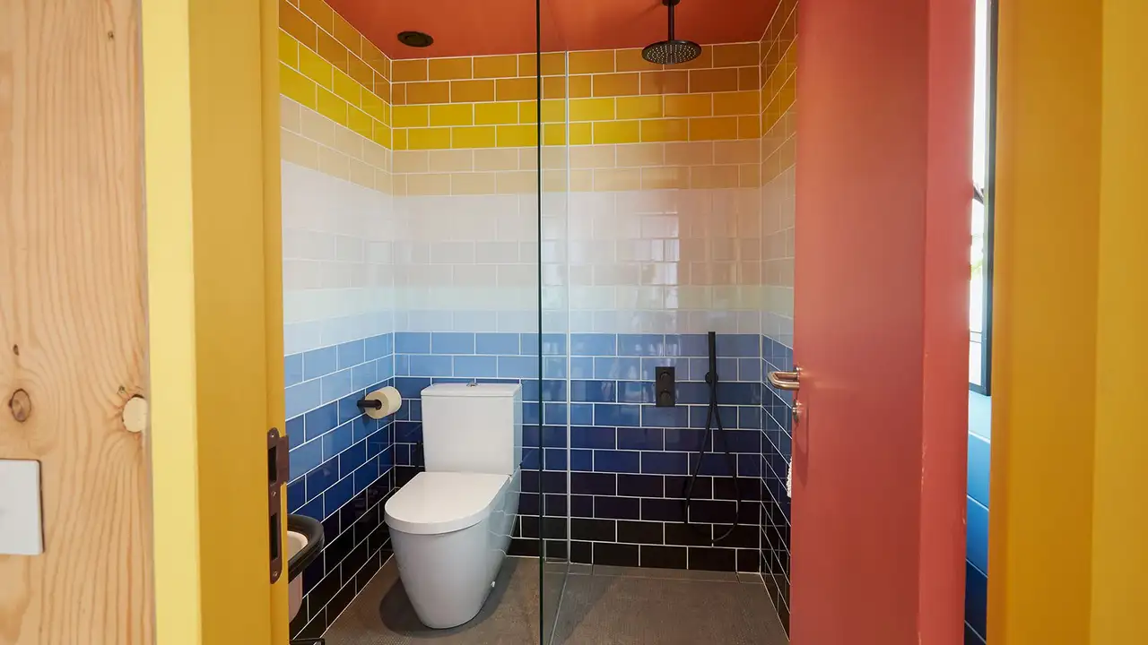 Fotografia de uma casa de banho colorida com base de duche e sanita, tirada a partir da entrada
