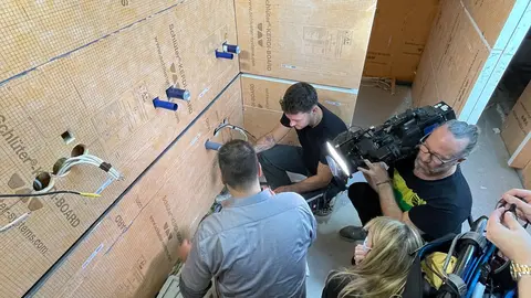 Uma equipa de filmagens filma dois trabalhadores a inspecionar os tubos de água e águas residuais que foram colocados.