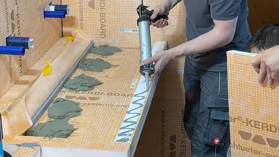Um instalador cola o lavat&oacute;rio personalizado feito de Schl&uuml;ter-KERDI-BOARD.