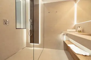 Casa de banho com cer&acirc;mica beige, duche ao n&iacute;vel do pavimento e lavat&oacute;rio com espelho grande