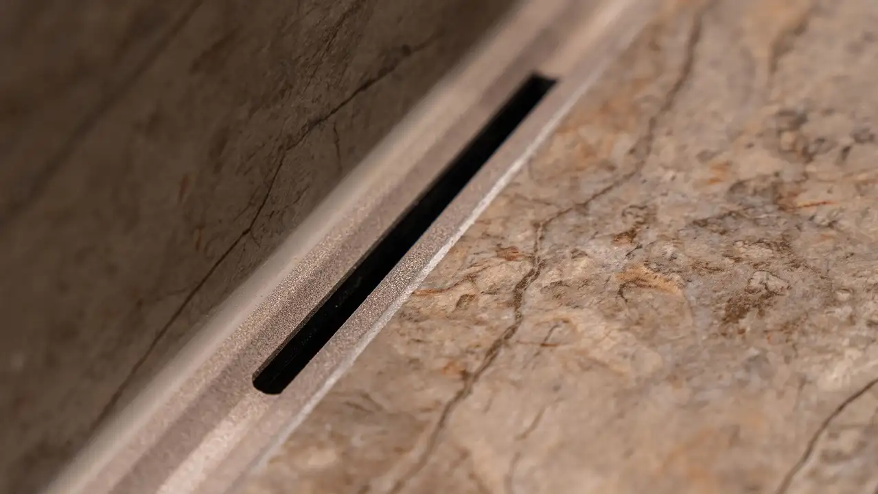 N&auml;rbild p&aring; linjeavloppet KERDI-LINE-VARIO installerat i tv&auml;ttst&auml;llet och med stengr&aring;, strukturbelagd yta