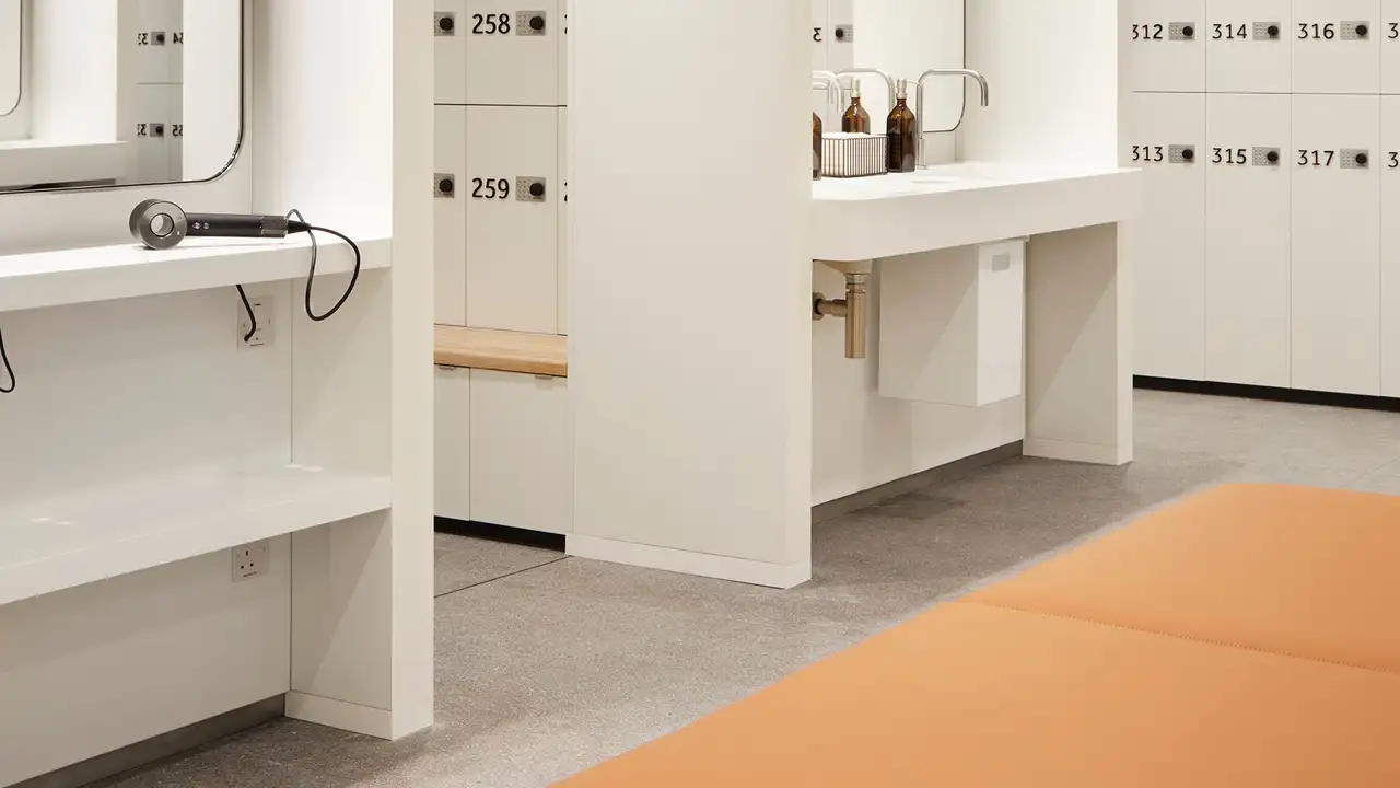 Omkl&auml;dningsrum i The JJ Mack Building med ljusgr&aring;a keramikplattor, orangef&auml;rgade sitsar och tv&auml;ttst&auml;ll