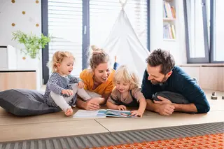 Familj med fyra personer ligger p&aring; golvet och tittar i en Schl&uuml;ter-broschyr.