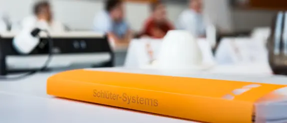 En orange mapp med texten Schl&uuml;ter-Systems ligger p&aring; ett bord
