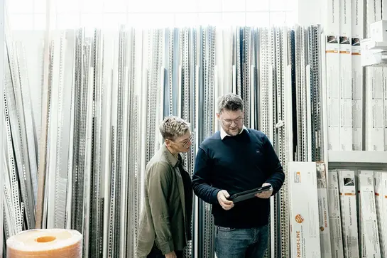 En utes&auml;ljare fr&aring;n Schl&uuml;ter-Systems i samtal med en kvinnlig kund framf&ouml;r en hylla med Schl&uuml;ter-produkter.
