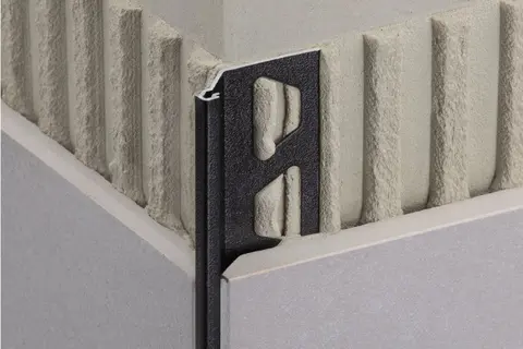 Detaljvy av kantskyddsprofilen Schl&uuml;ter-FINEC med TRENDLINE-bel&auml;ggningen MGS grafitsvart matt p&aring; ett gr&aring;kaklat v&auml;ggytterh&ouml;rn