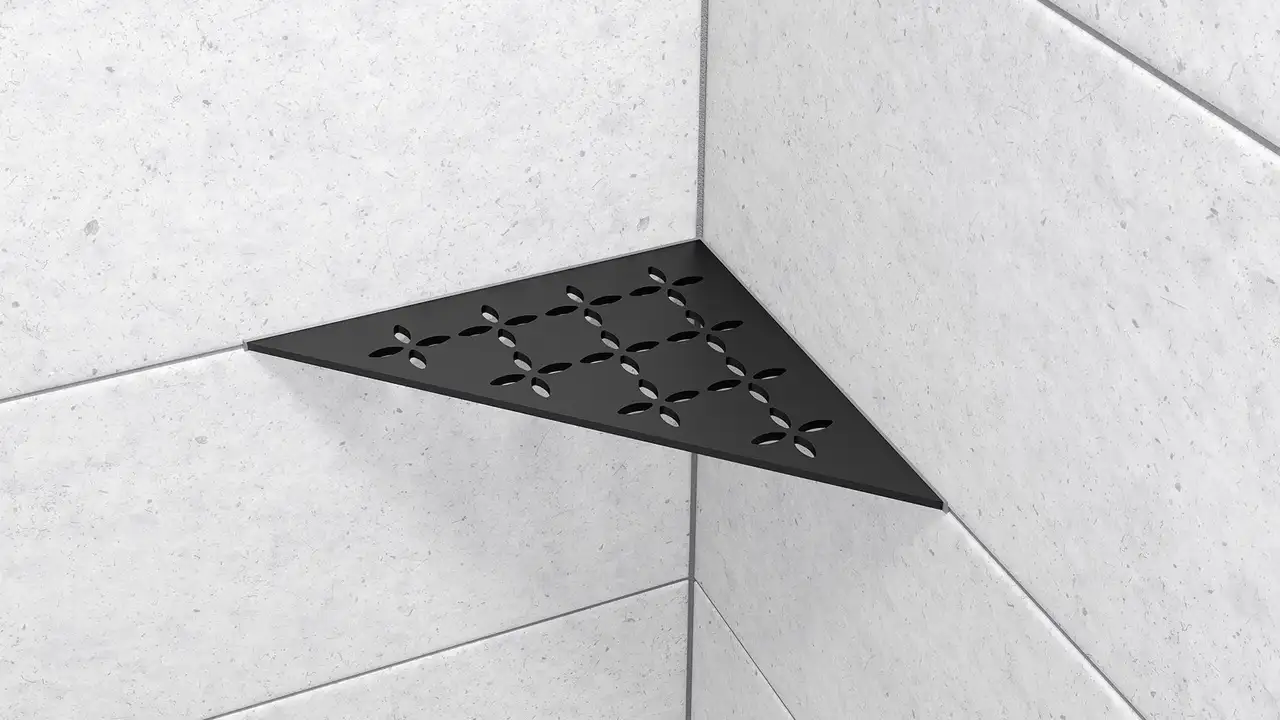 H&auml;r visas en produktn&auml;rbild p&aring; duschh&ouml;rnhyllan Schl&uuml;ter-SHELF-E-S1 i form av en liksidig triangel i designen FLORAL MGS grafitsvart matt installerad p&aring; ljusgr&aring;tt v&auml;ggkakel.